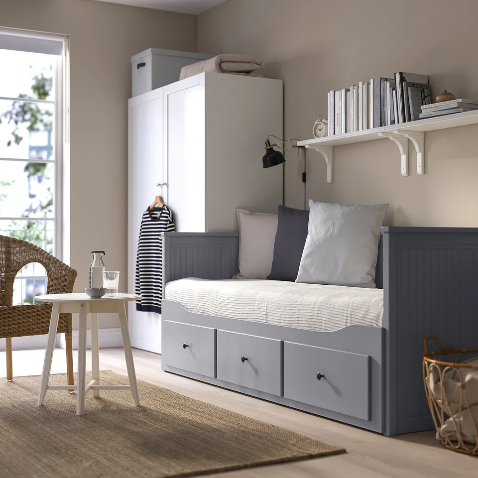 Modern bedroom with HEMNES day-bed, bookshelf, small table, ironing board, and corner chair.