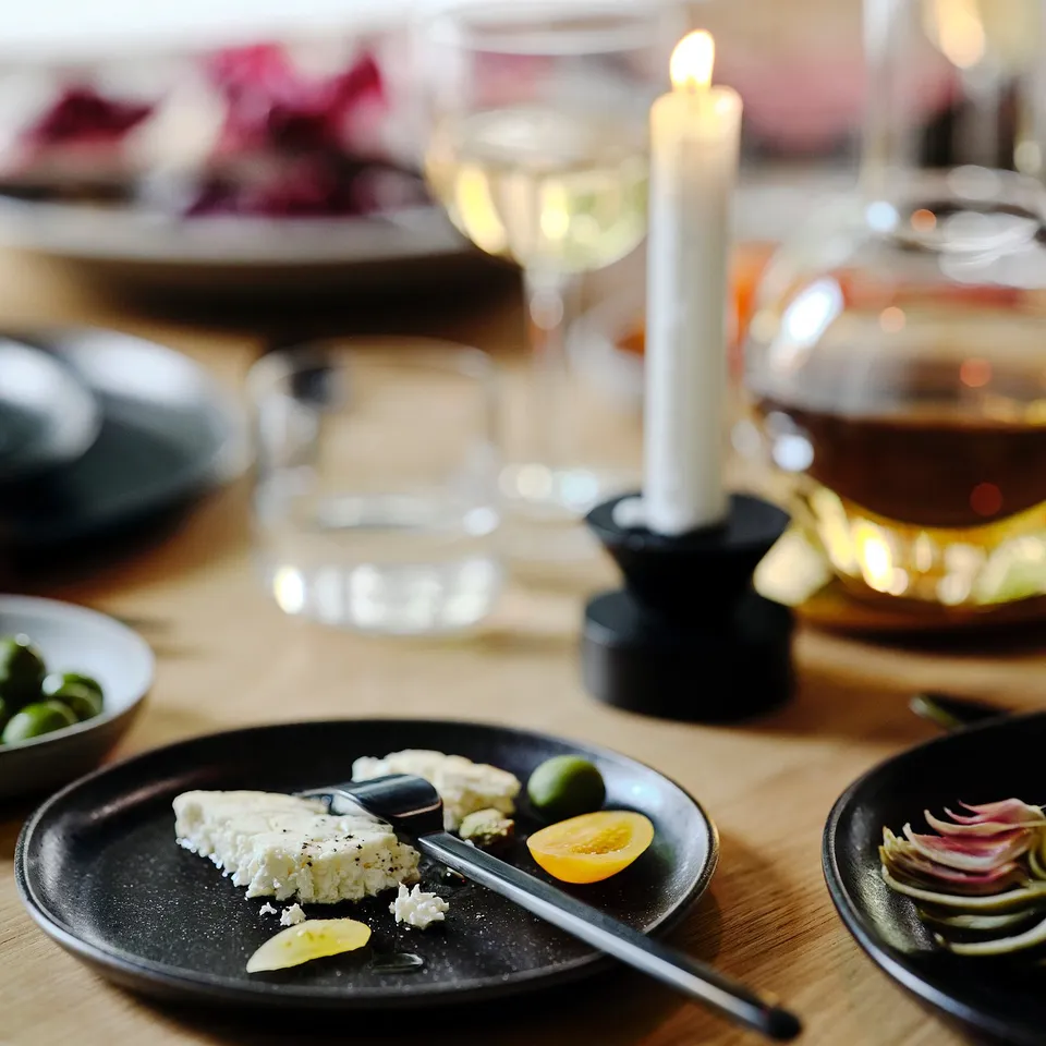 Black plate with cheese, lemon, olives, candle, glass, wine. Rustic, elegant table setting.