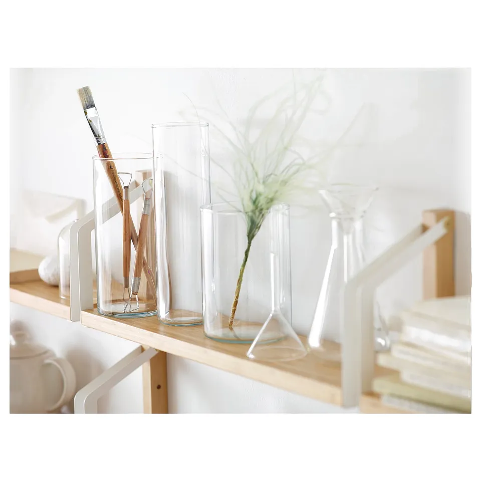 Clear glass CYLINDER vases in different sizes on wooden shelf; one holds paintbrushes, another has a green plant.