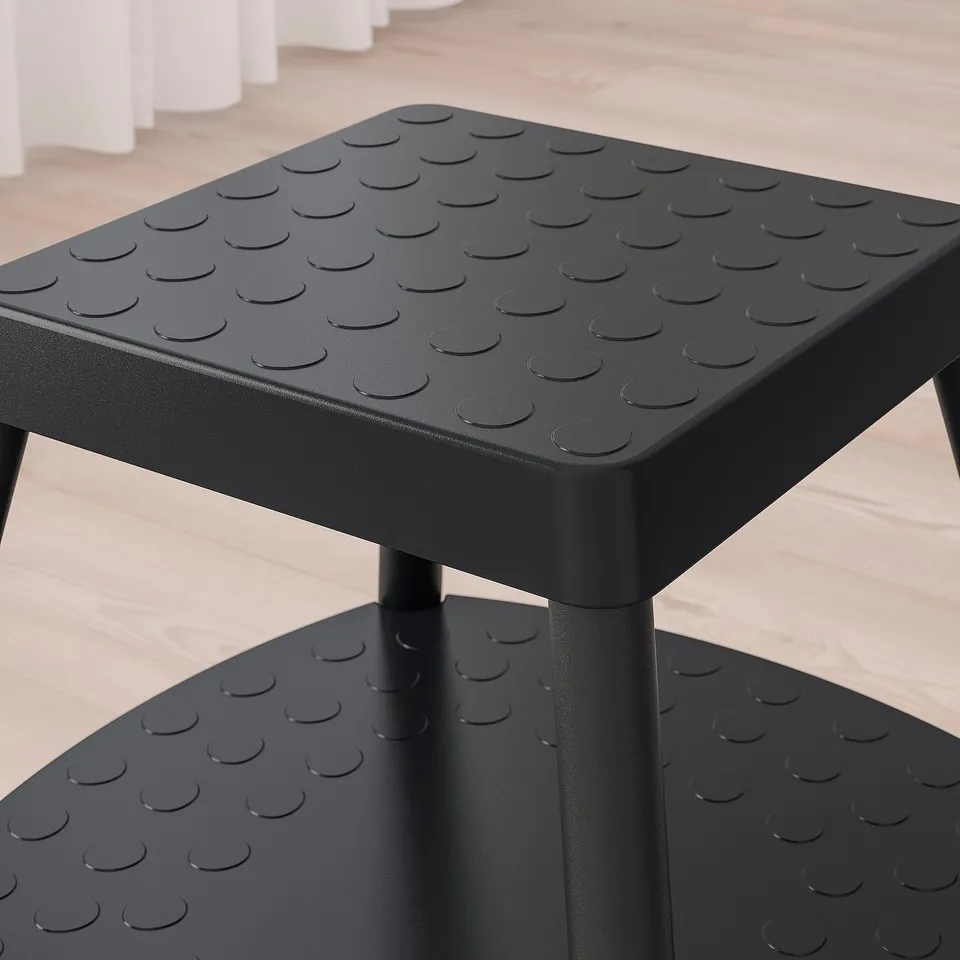 Black step stool with patterned textured surface, sturdy metal legs, two wide steps for stability.