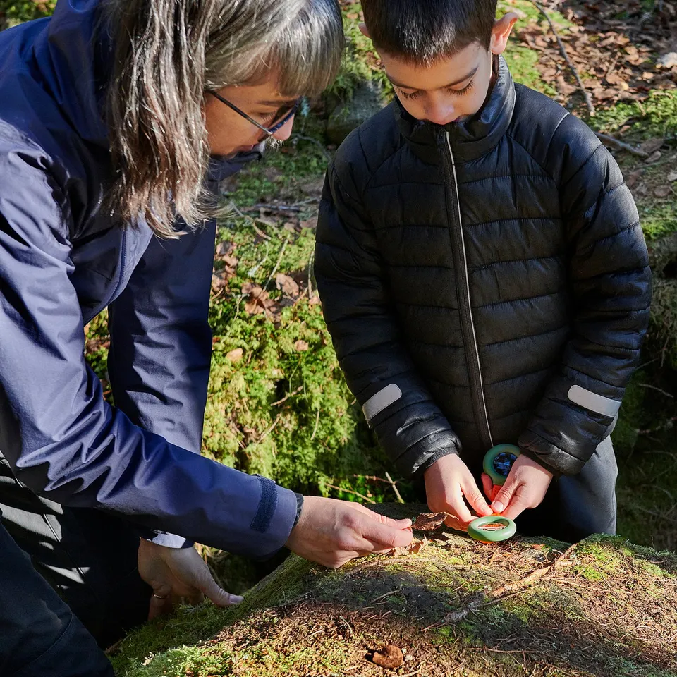 Adult and child explore nature with MAJBAGGE tools: compass and magnifying glass.