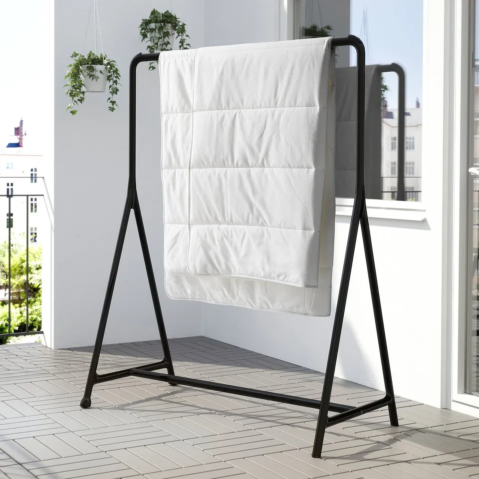 Black metal drying rack with white blanket hangs indoors near window.