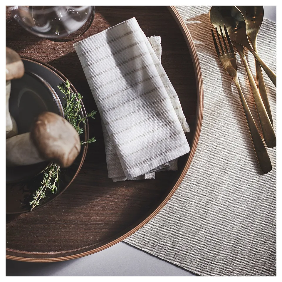 Round wooden tray with golden utensils, white striped napkin, and dish with herb garnish.