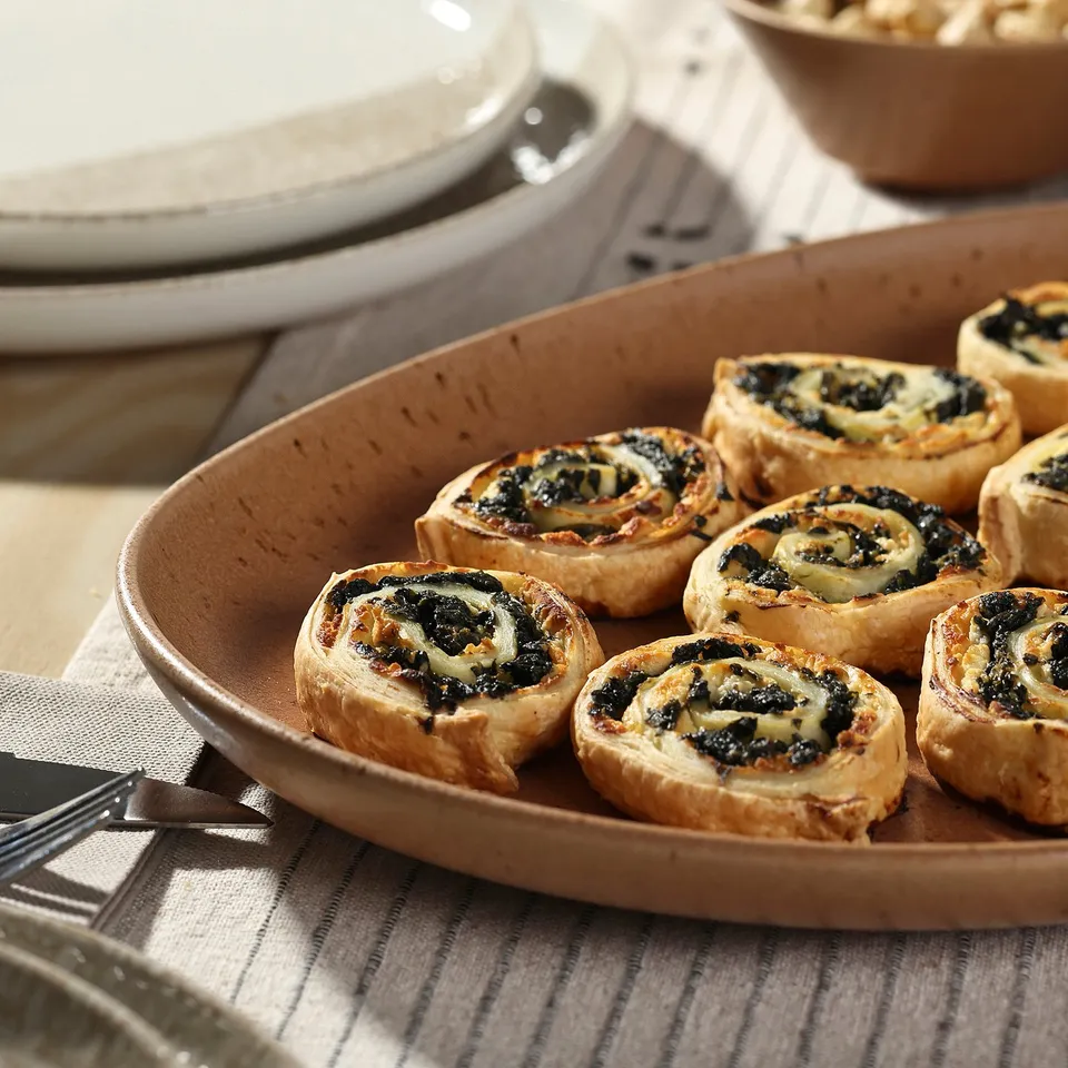 Rustic GRÅRÄV grey stoneware plate holds eight spinach tarts, with a stack of plates behind.