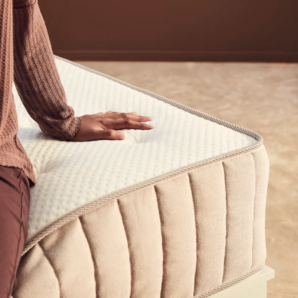 A person in brown clothes tests a white and beige mattress, checking comfort and support.