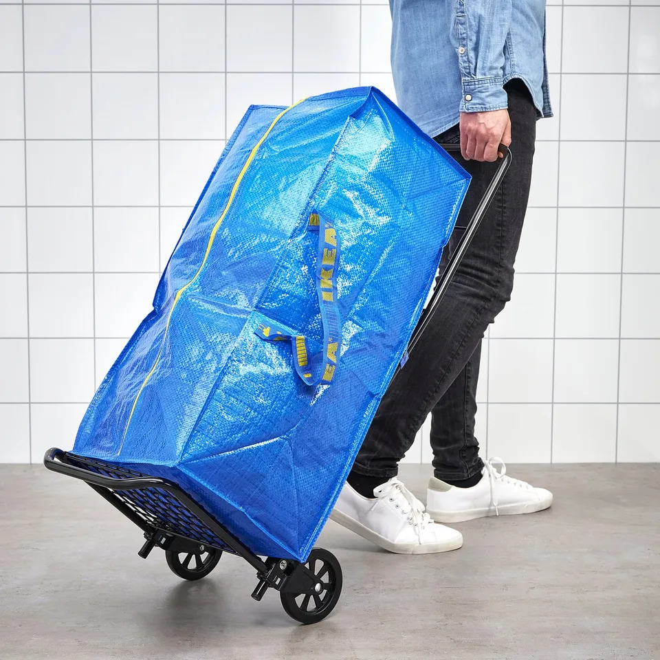 Person pushing blue FRAKTA bag on wheels, designed for carrying and storing large loads.