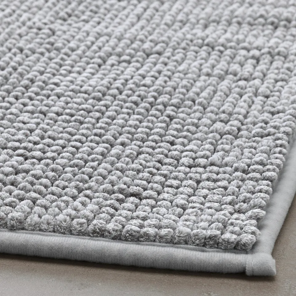 Soft, light grey bath mat with textured, circular patterns, great quality, lying on a flat surface.