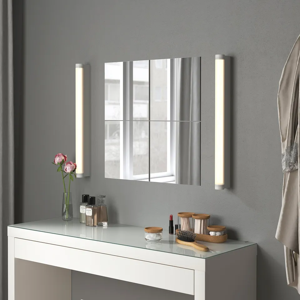 White BLODLÖNN mirror with lights, above cabinet with cosmetics, flowers, towel. Segmented, modern bathroom look.