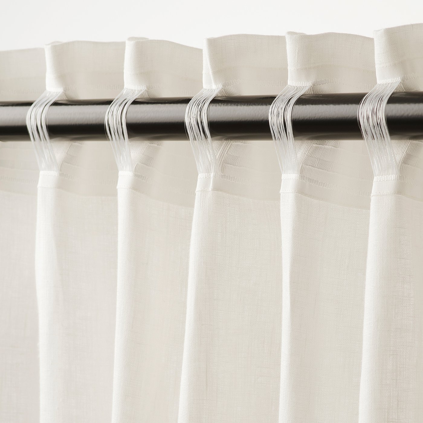 White curtains hang with pleats, allowing light through while providing privacy. Metal rod and hooks visible at the top.