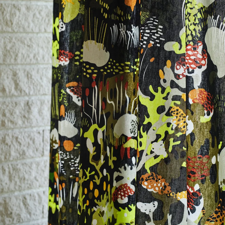 Vibrant, patterned curtain with nature themes hangs near white brick wall.
