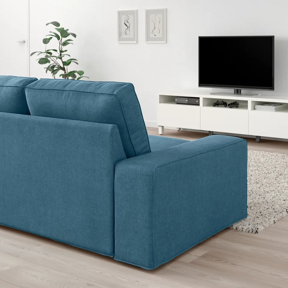 Blue KIVIK sofa with low armrests, 10-year guarantee, against white wall with tv and plant.