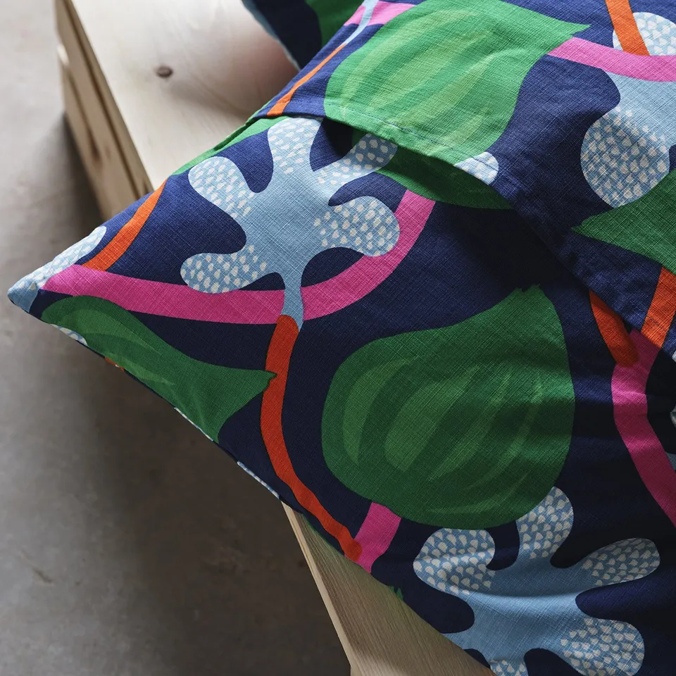 A colourful, patterned cushion cover with large leaves and green apples, featuring hand-embroidered details on a sofa.