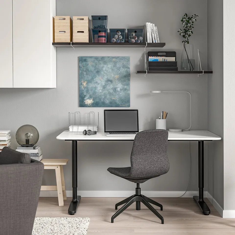 Modern home office: black desk with laptop, grey chair, wall shelves with books & decor.