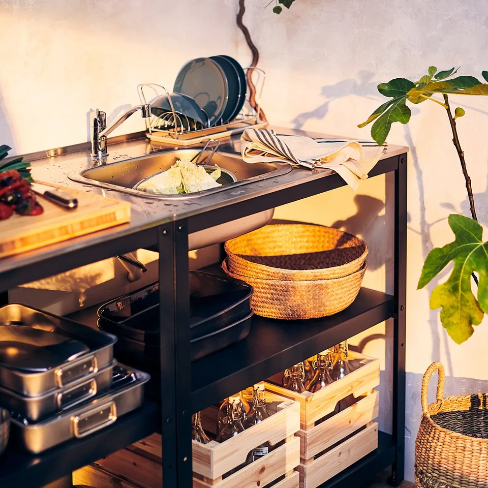 Modern outdoor kitchen with black sink, wicker baskets, wooden crates, and plants.