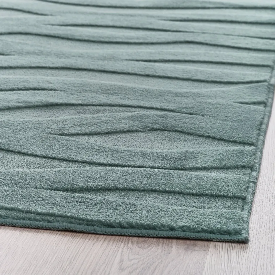 Close-up of a soft, lightly textured blue rug with 3d waves, lying on a wooden floor.