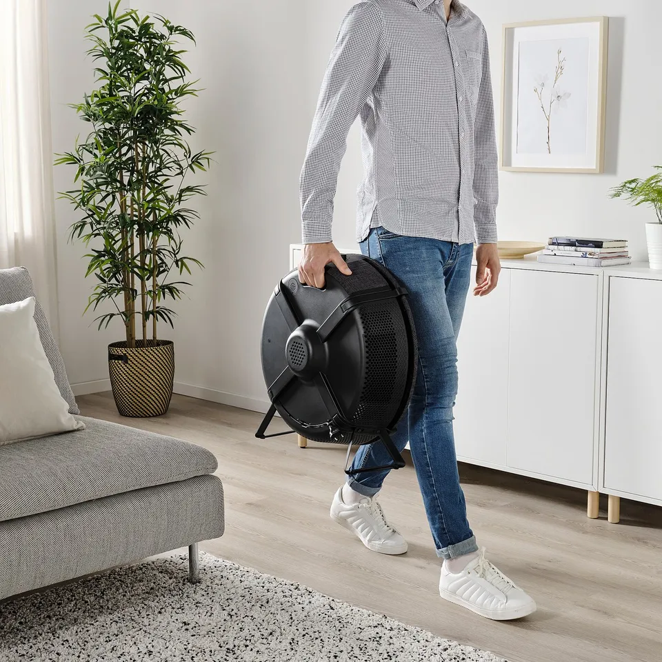 Person holding a portable air purifier in a living room. The person is adjusting it near a couch and a cabinet.