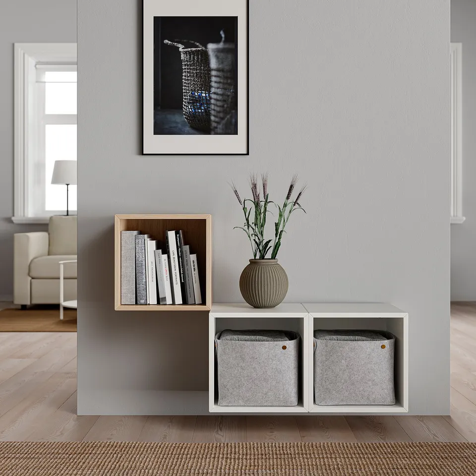 Modern living room with white EKET shelves holding books and a vase with plants. A framed picture hangs above.