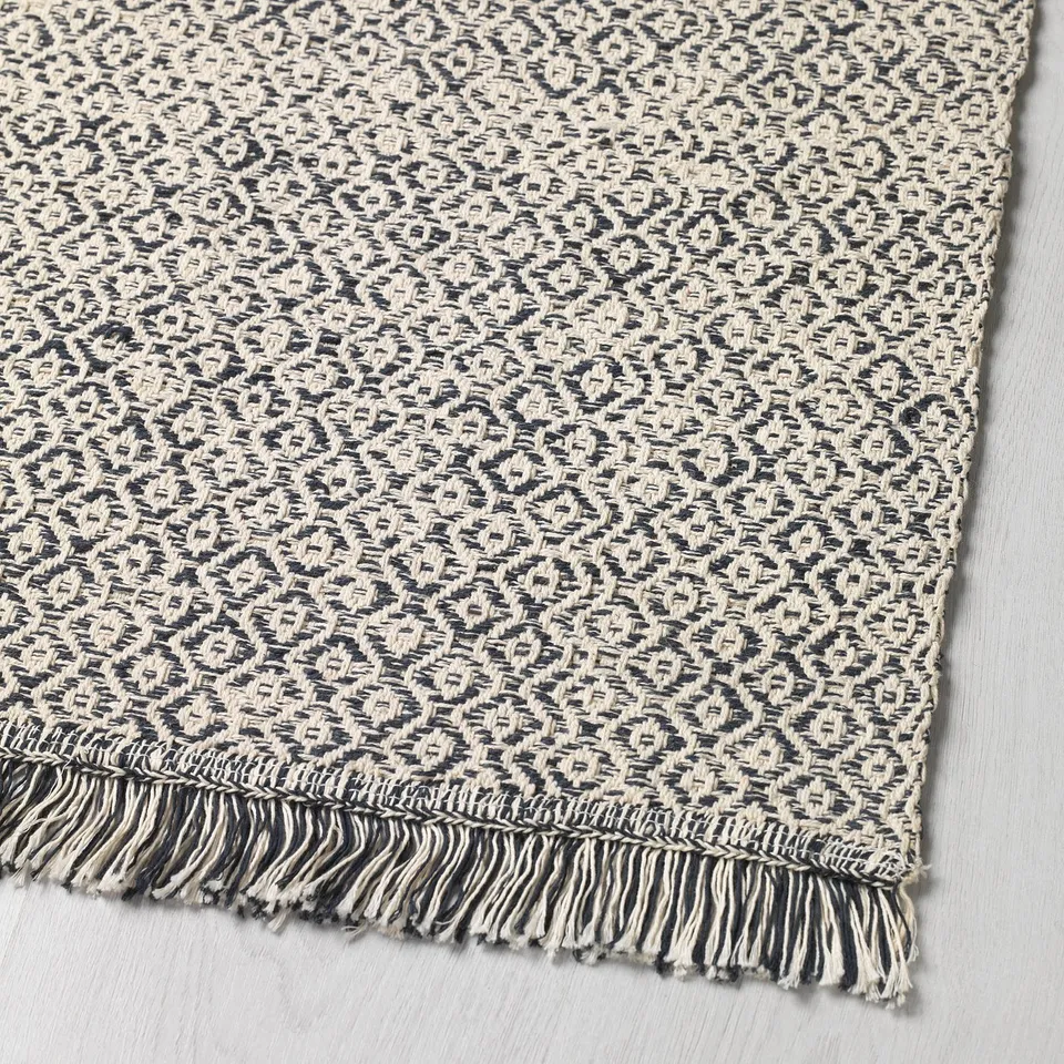 Textured, black-and-white woven rug with fringe edges, displayed on a flat surface.