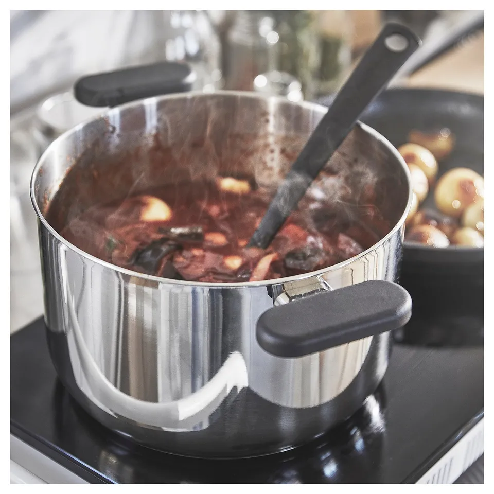Stainless-steel saucepan with black handle, boiling food on stove, steam visible.