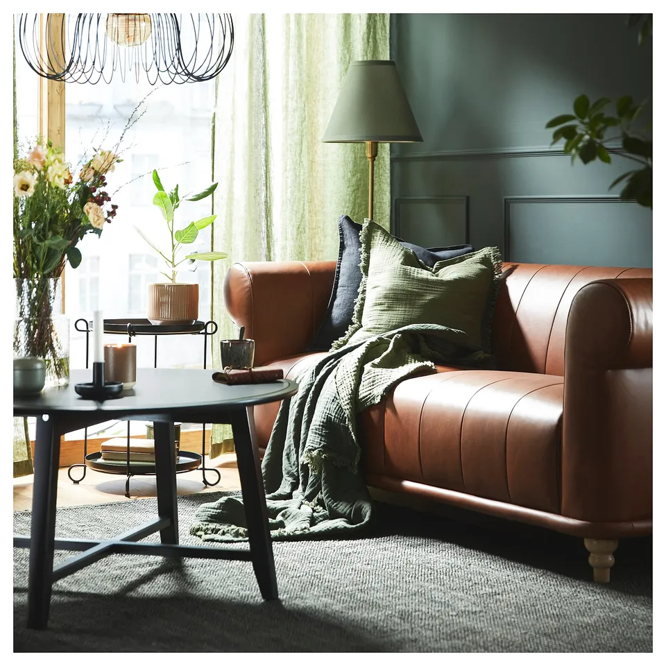 Stylish living room with dark green LANDBANA jute rug, brown leather couch, green lamp, and black coffee table with decor.
