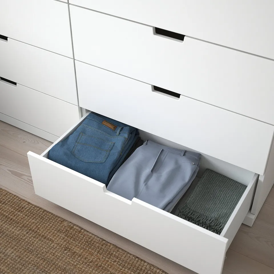 Open white NORDLI drawer revealing folded jeans and trousers, showcasing organised storage.