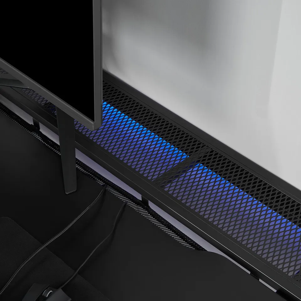 Black gaming desk with blue lighting under mesh, supporting monitor and pc, showcasing adjustable height legs and cable management.