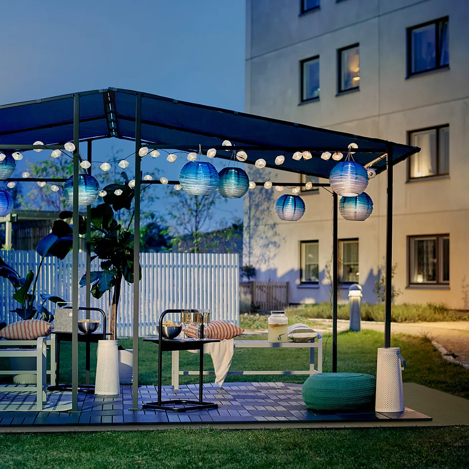 Modern outdoor patio with blue-lit GUNNÖN pergola, offering shade and ambiance with lights.