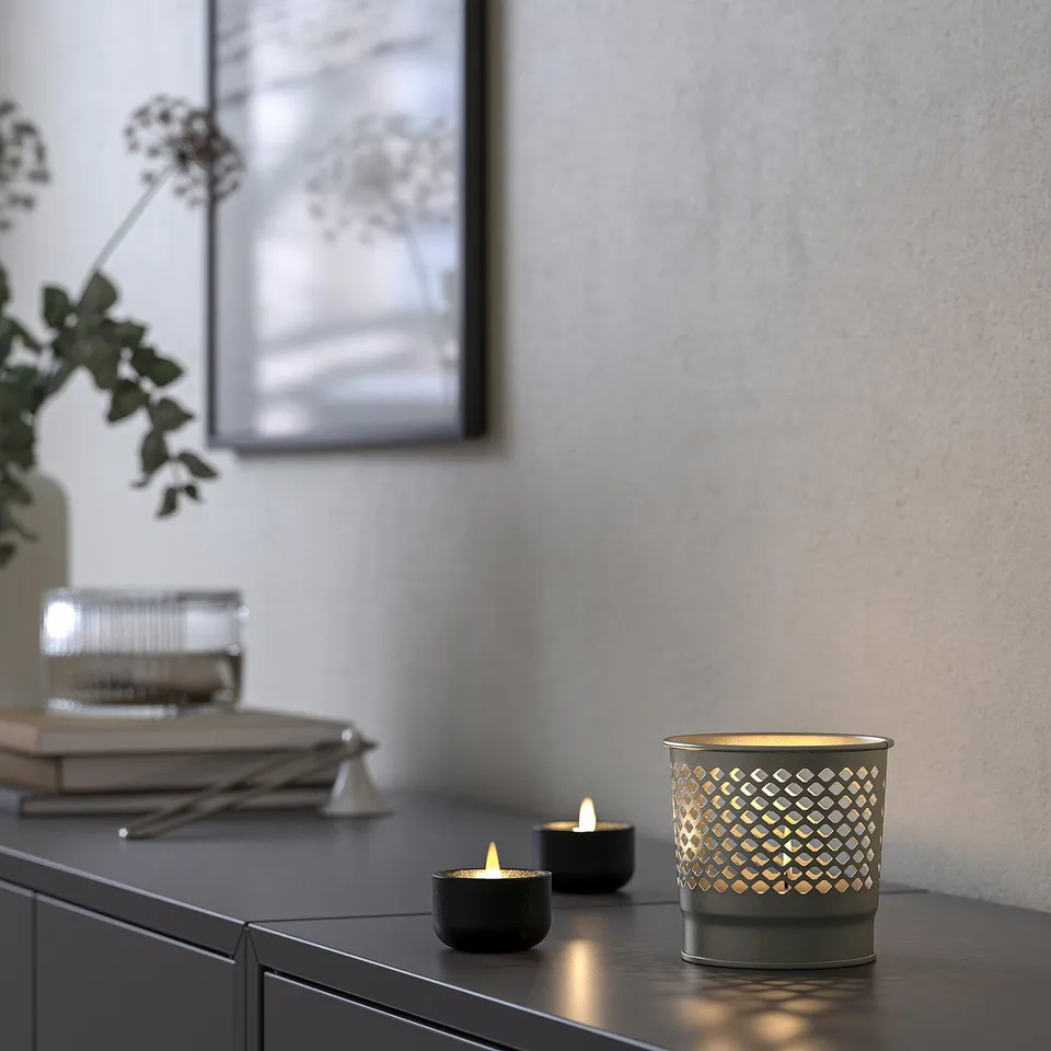 A dimly lit room candle holders on a table, casting decorative patterns on the wall. One large holder illuminates softly, creating a cosy atmosphere.