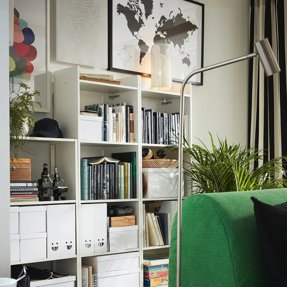 Modern home office with white BAGGEBO bookcases filled with books and storage boxes, featuring a green chair with a black cushion.