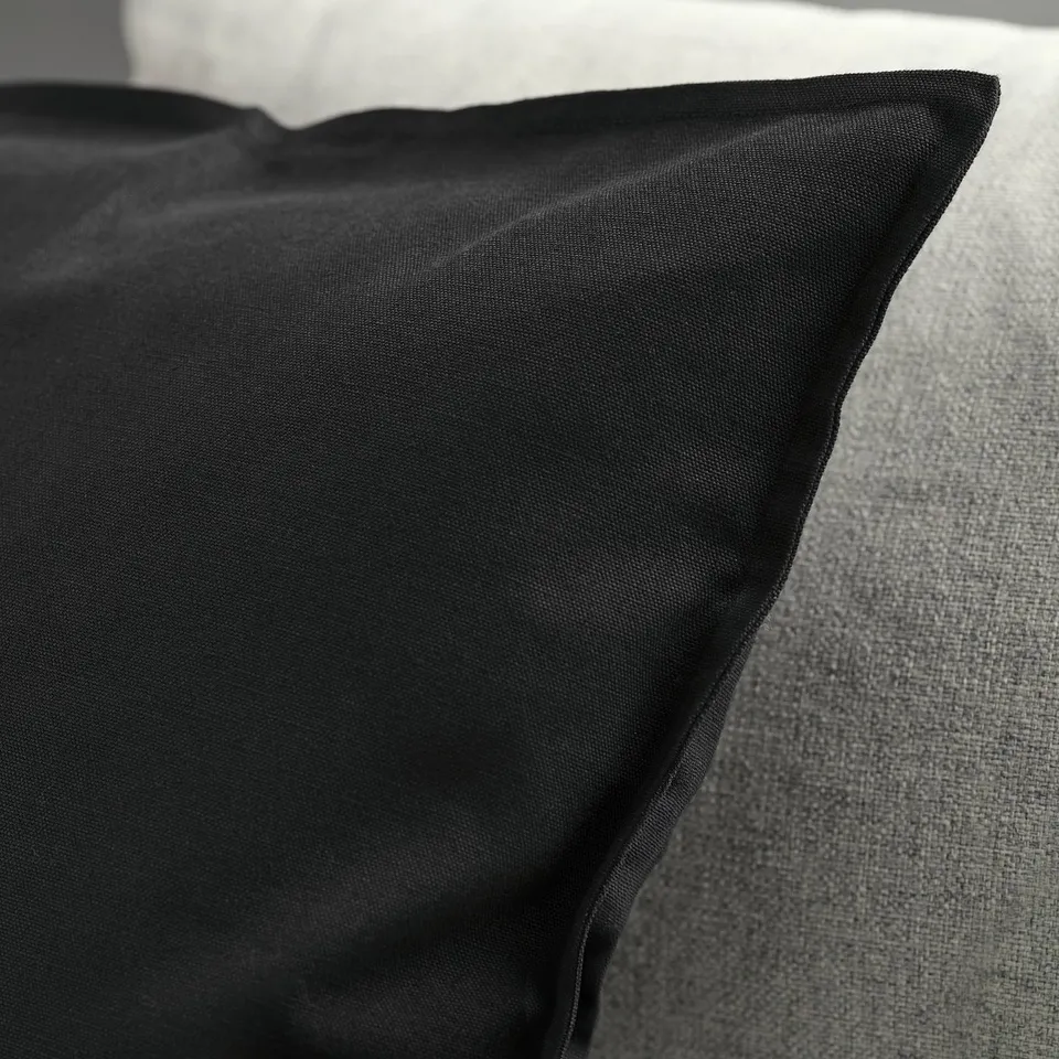 Black cushion cover on a grey surface, showing smooth texture and neat stitching.
