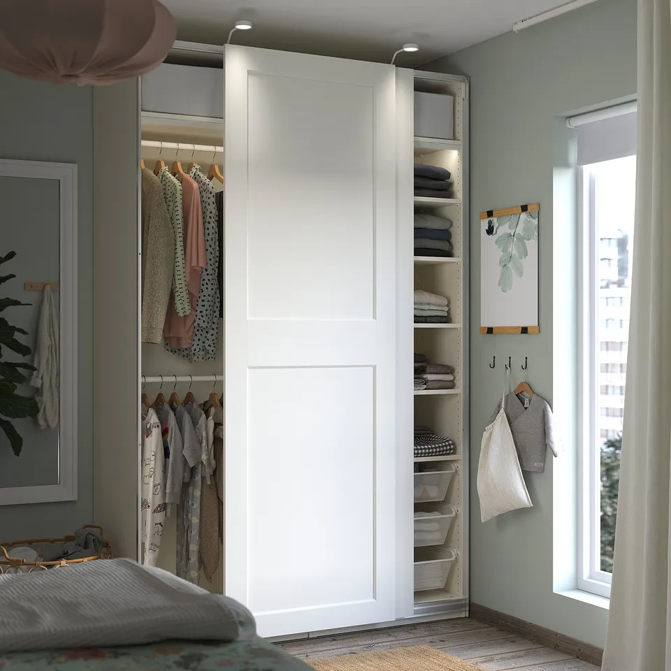 Neat bedroom with white IKEA PAX wardrobe, its sliding doors open to reveal clothes and shelves, colourful decor around.