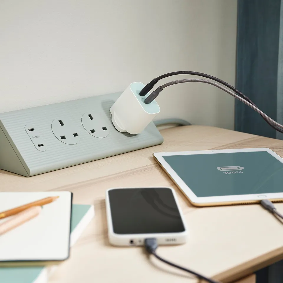 Desk setup with SJÖSS charger, smartphone/tablet, notepad, and pencils against a light wall.