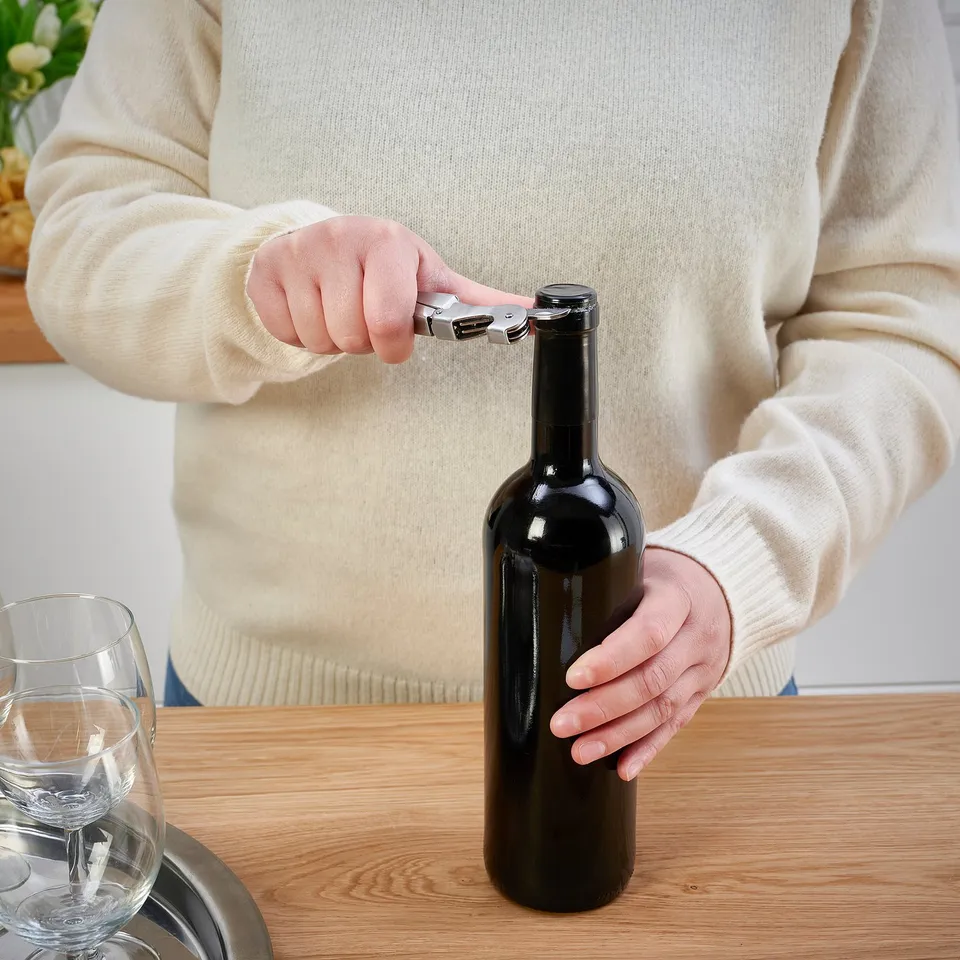 Person in cream sweater using corkscrew to open wine bottle.
