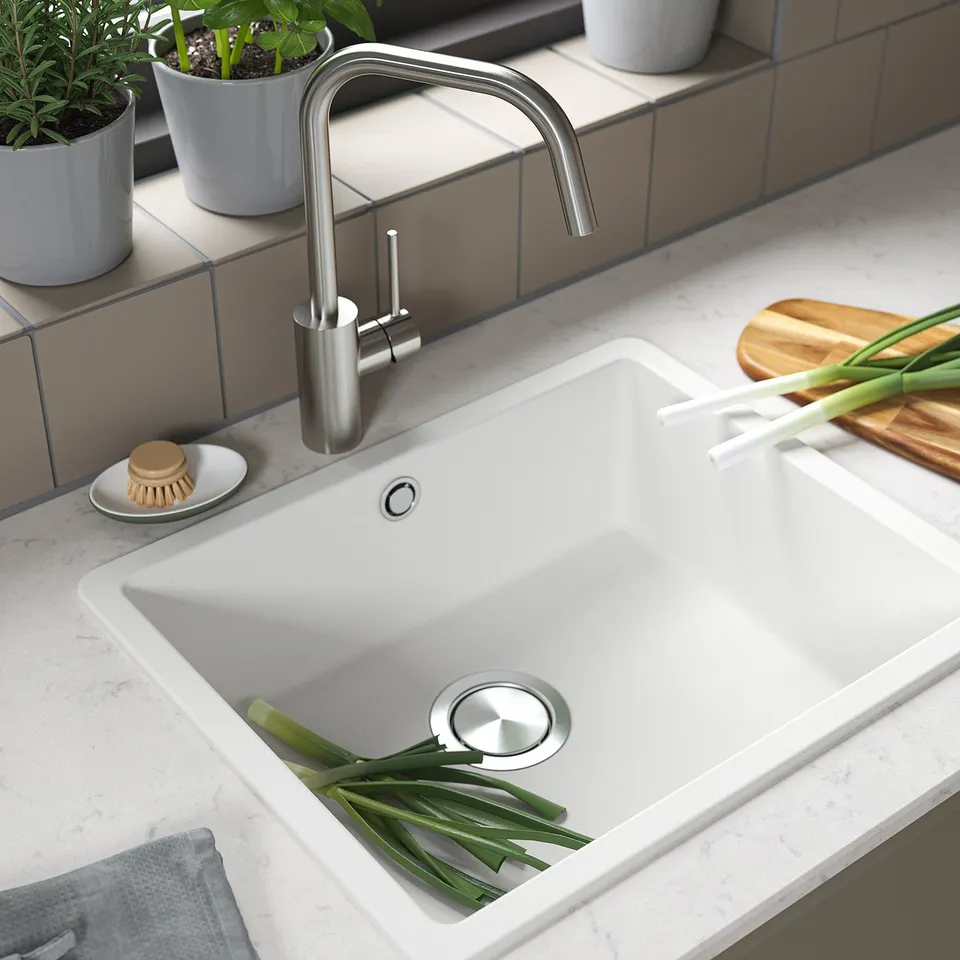 White quartz sink with stainless steel tap, green onions, plant, cutting board.