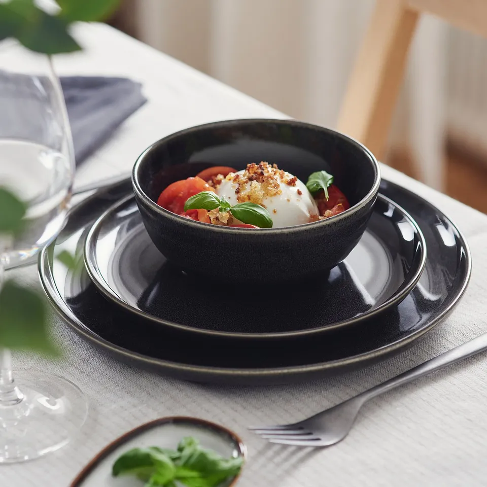 Dark grey glazed bowl on stacked plates, holding fresh tomatoes, mozzarella, and basil. Ideally used for serving and displaying food.