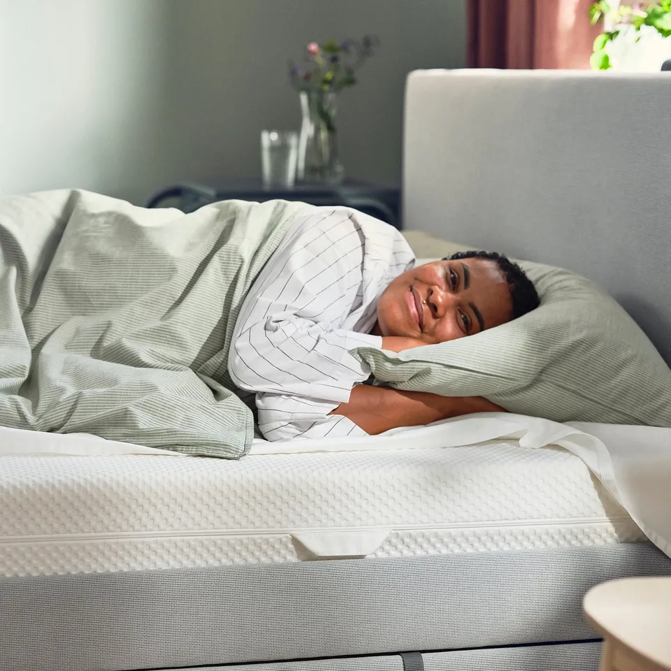 Person sleeping peacefully on a white mattress with striped grey sheets. A cosy bedroom setting.