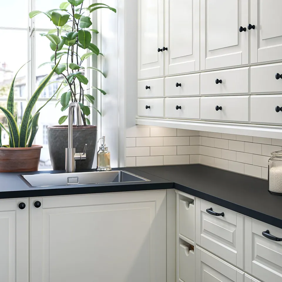 A modern kitchen with white cabinets, black countertops, and potted plants near a window.