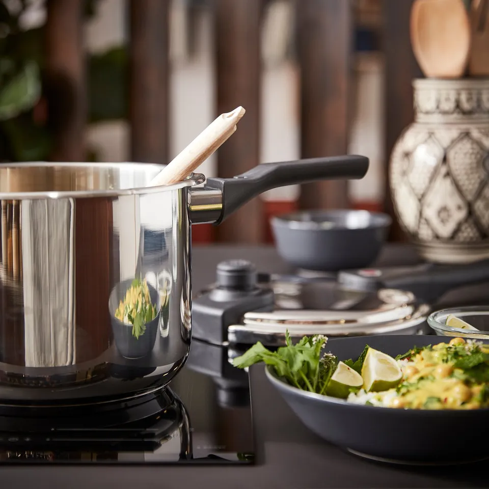Stainless steel pressure cooker on stove with lid, bowl of green salad, lime slices, and black handles.