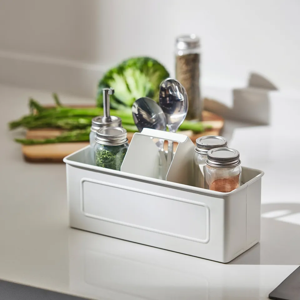White kitchen caddy with handle holds jars and utensils, keeping counter neat.