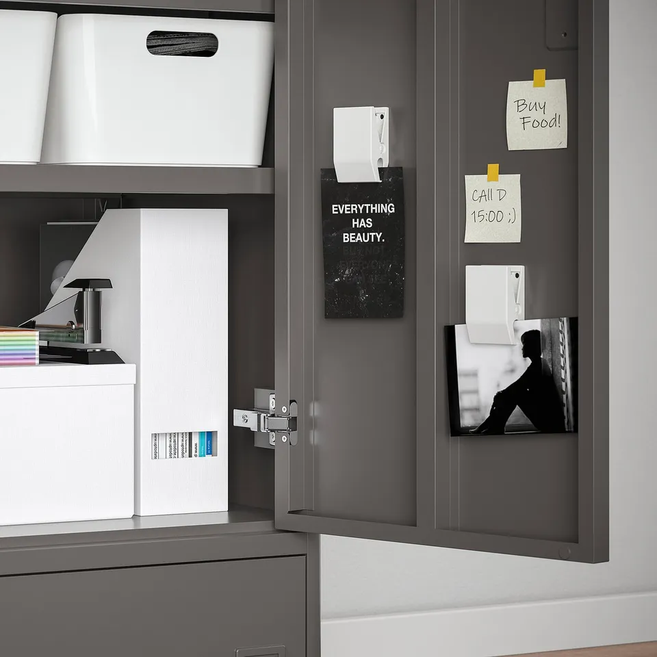 Open grey cabinet displaying organised storage: white bins, notes, and motivational poster.