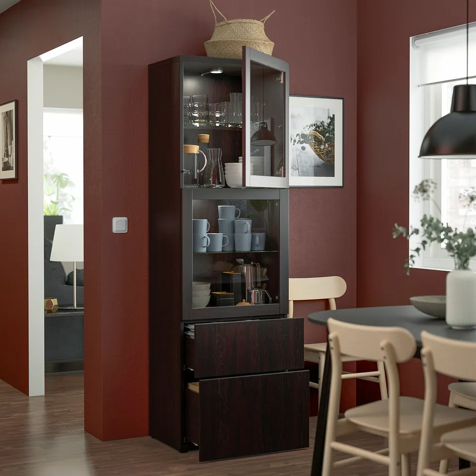 Dark wooden BESTÅ cabinet displays items on glass shelves with closed drawers at base.