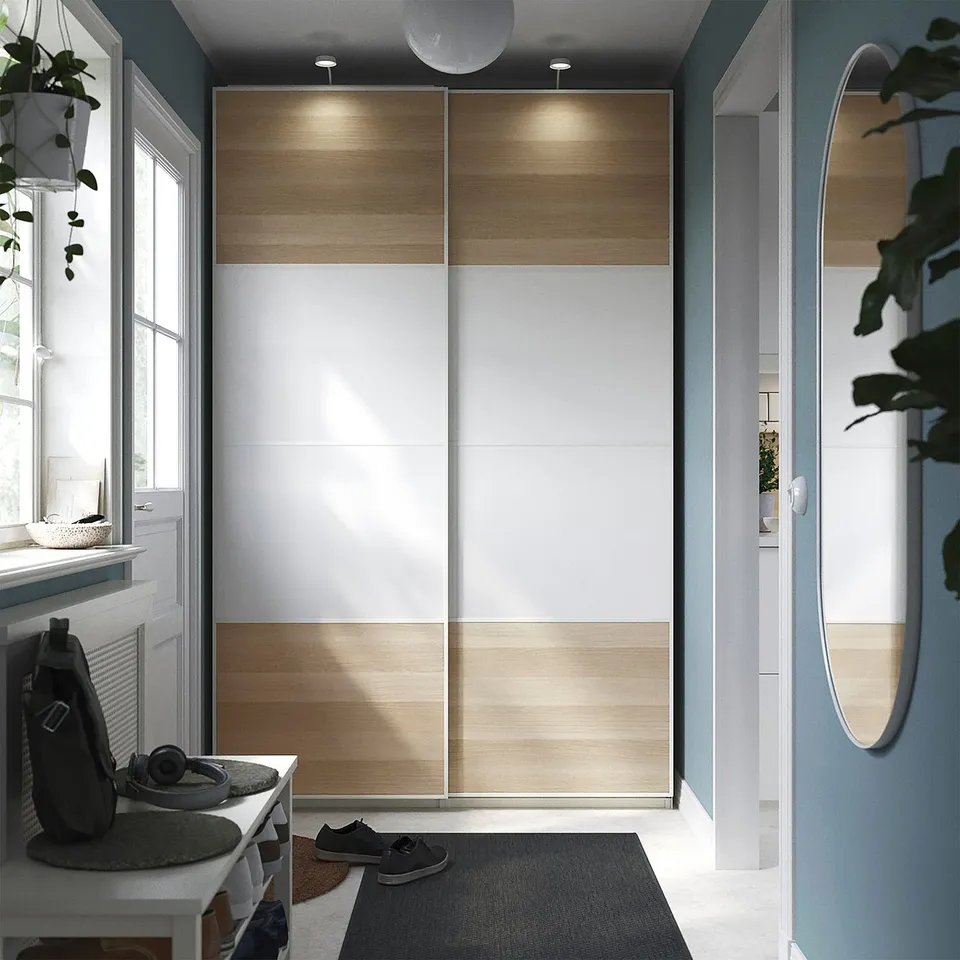 Modern wardrobe with sliding doors, wood and white panels, integrated lighting, blue wall, window, side table.