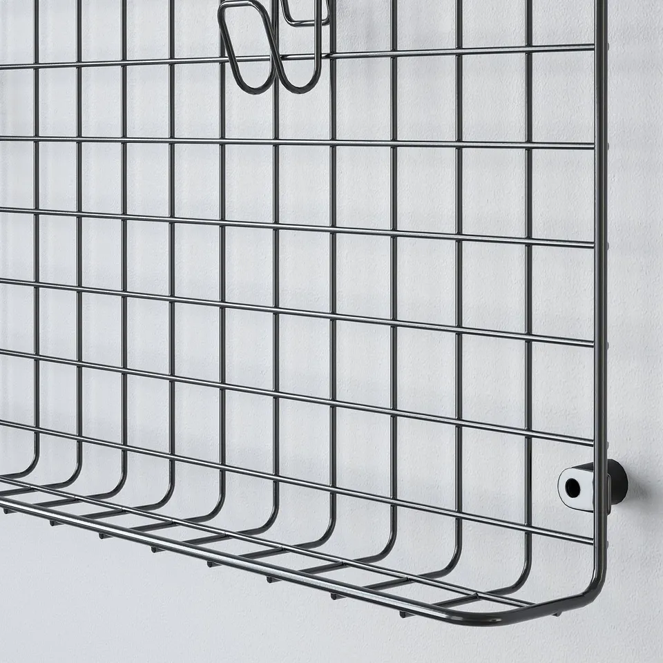Black metal wall shelf with multiple small compartments and hooks, mounted on a white wall.