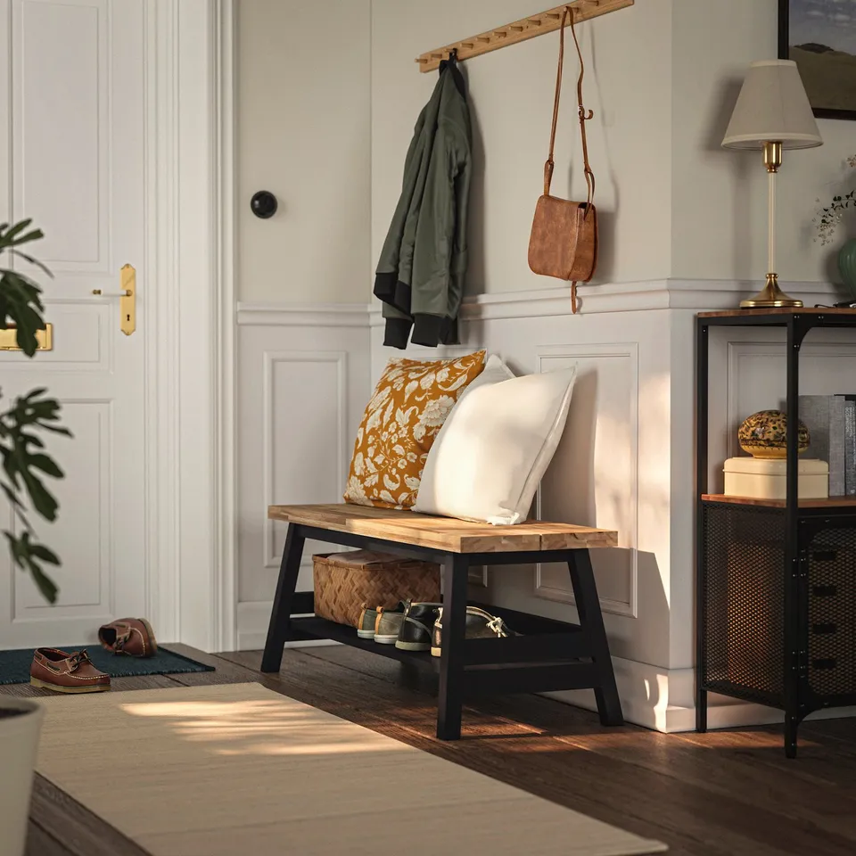 Wooden SKOGSTA bench in hallway, natural & black, coat rail above, lamp beside, shoes underneath.