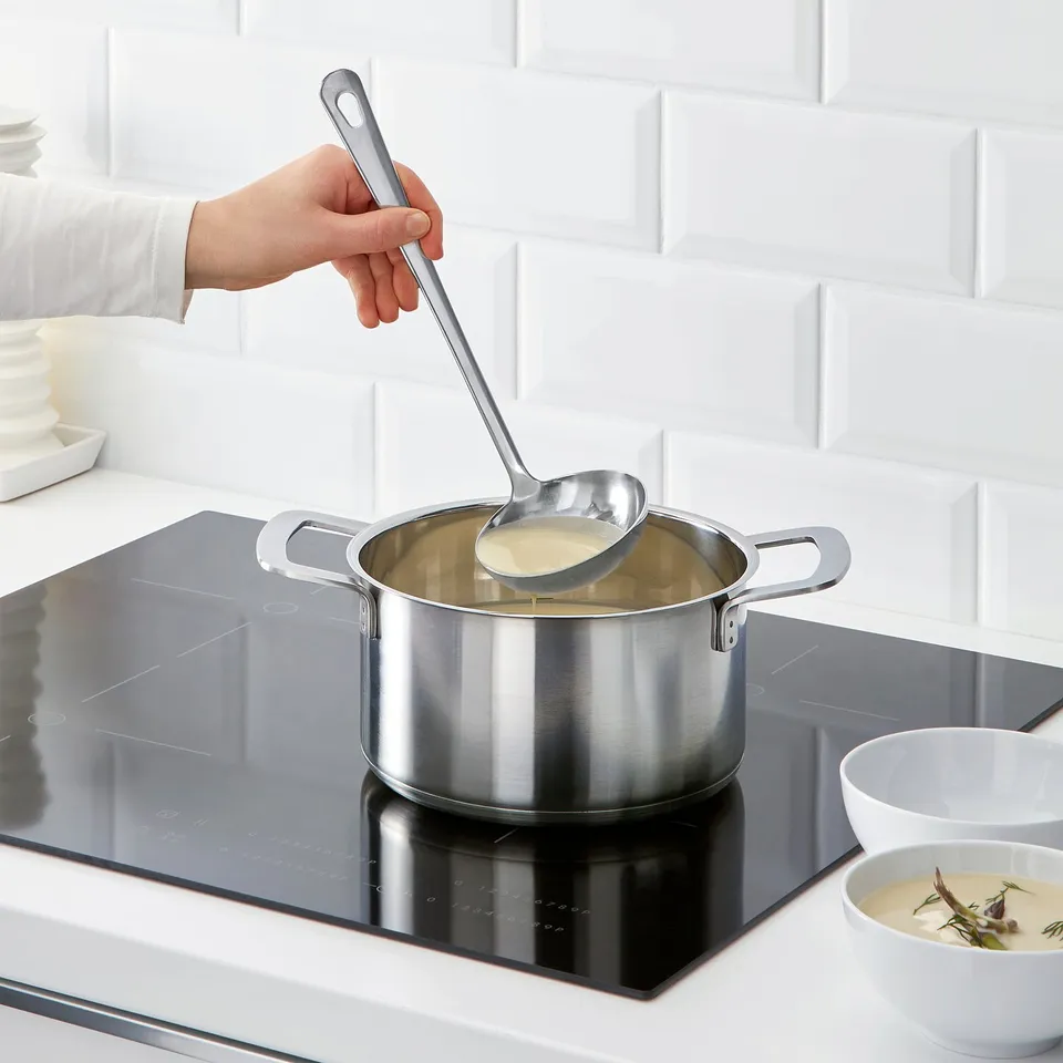 Ladling soup on induction stove in modern kitchen.