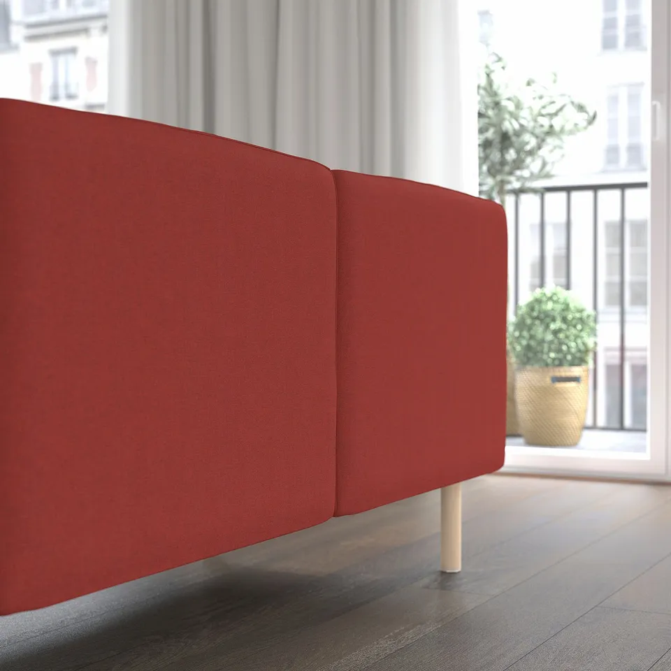 Red modular sofa with wooden legs near a window offering comfort and flexibility.