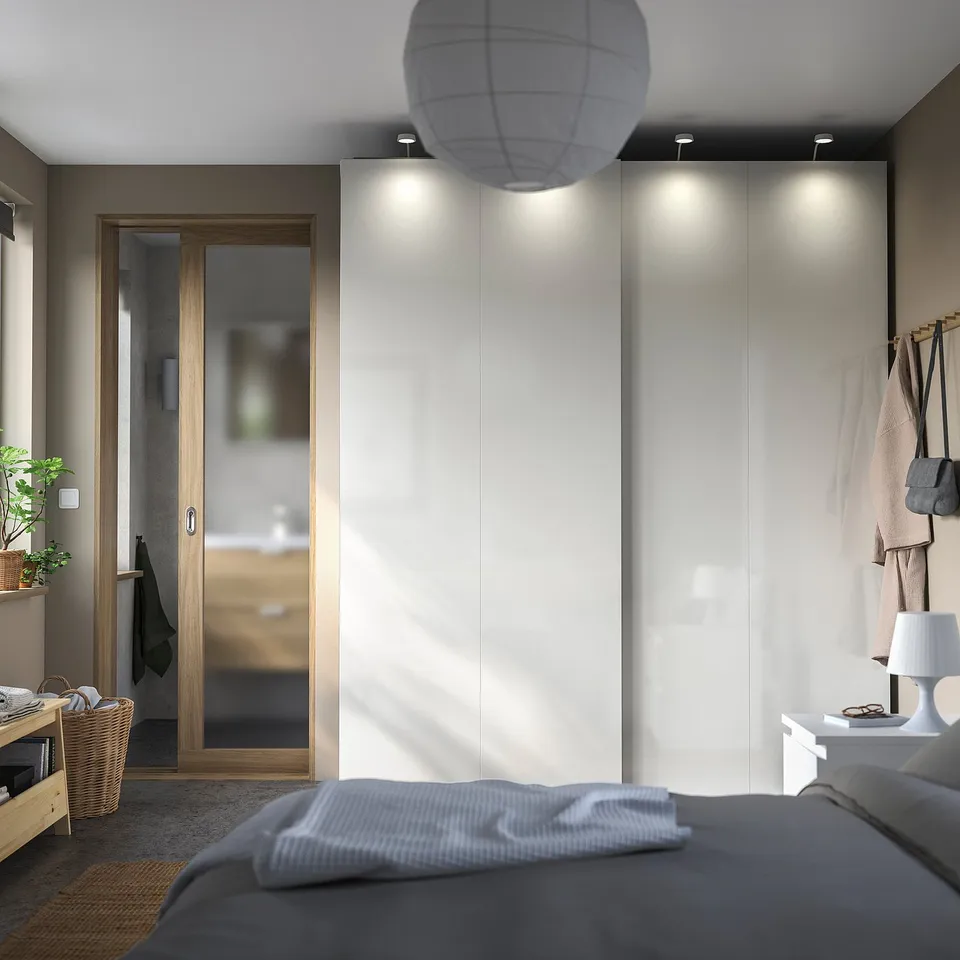 Bedroom with white HASVIK sliding wardrobe doors, grey bed, and hanging bags.