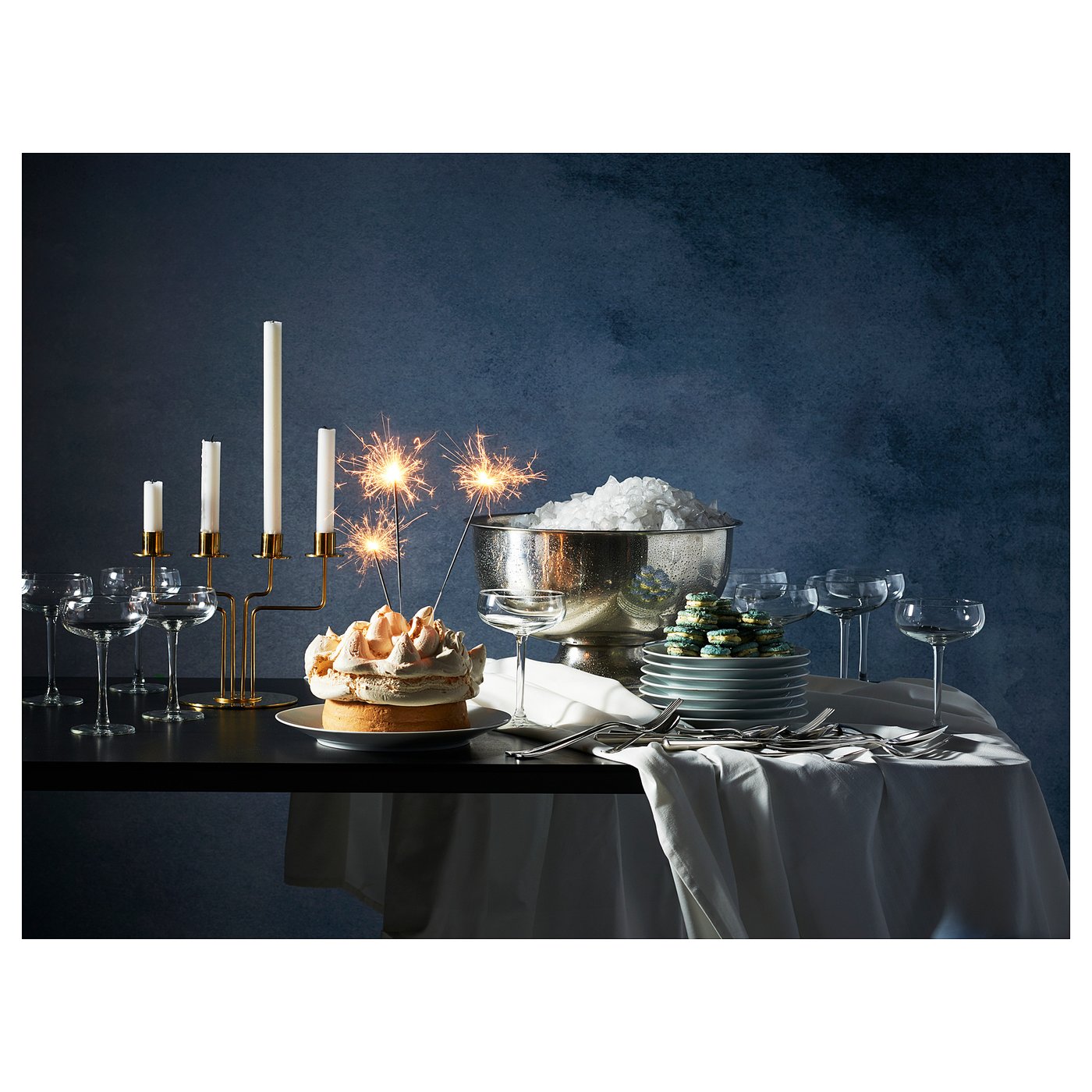 Elegant table setting with sparklers and cake, lit by a golden candelabra with four candles, set against a dark background.