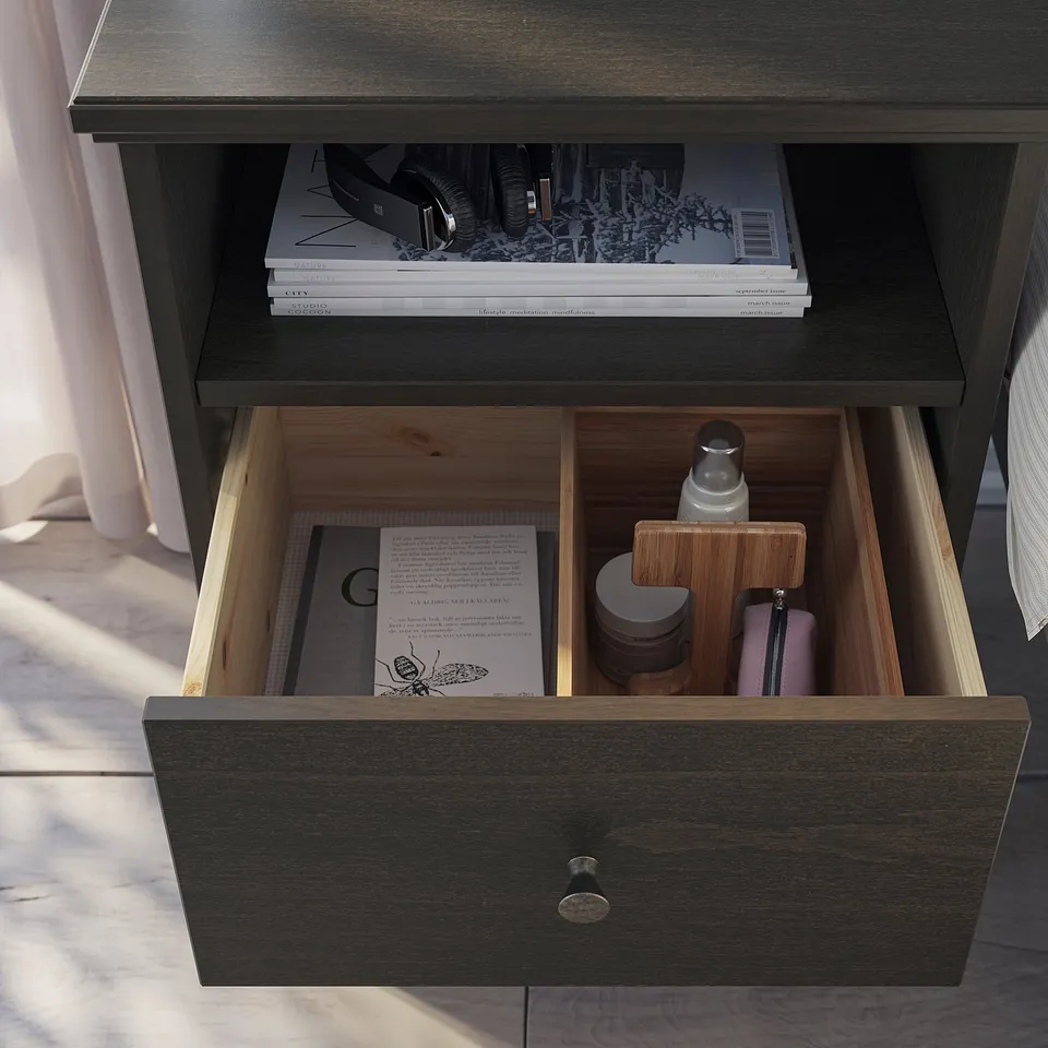 Dark wood bedside table, open top with books, bottom drawer open revealing organiser with containers and a book.