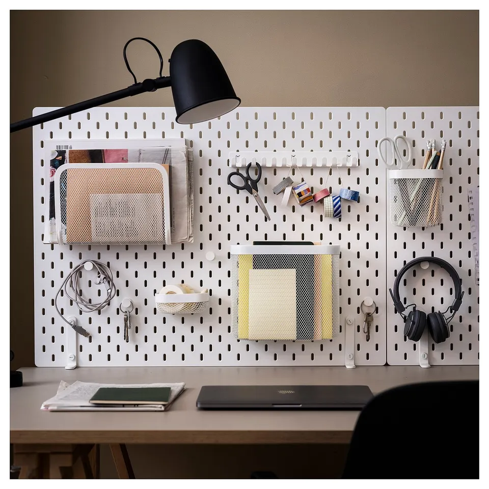 Desk setup with white SKÅDIS pegboard organising office supplies, lamp, and headphones.